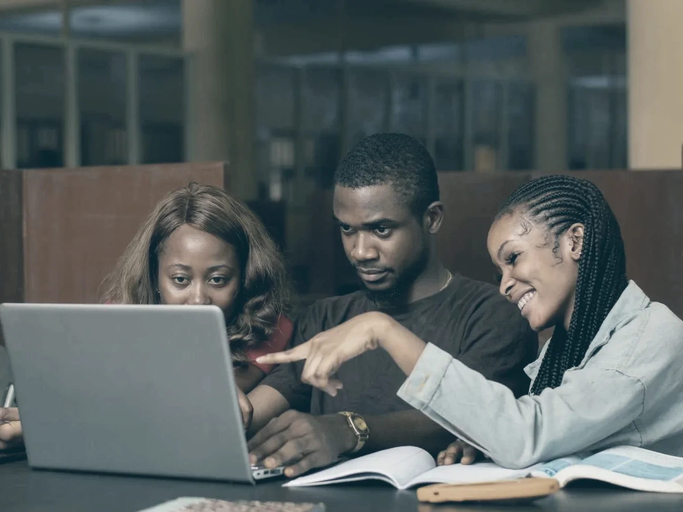 Three students working together around a laptop in a library
