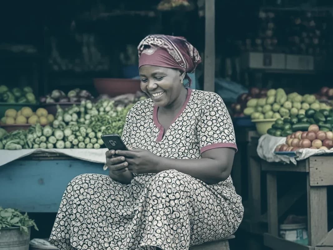 A market trader smiling at her phone beside her produce stall