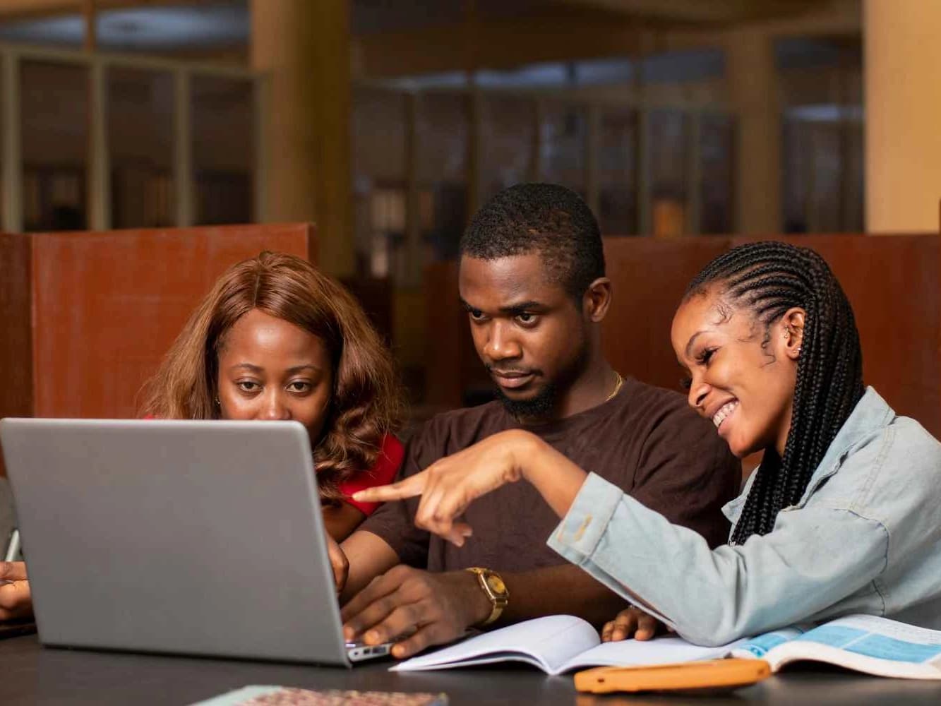 Three students working together around a laptop in a library
